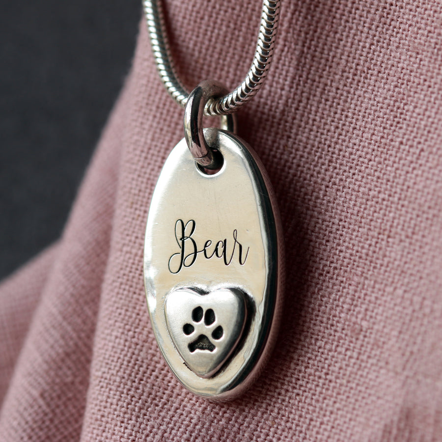 Silver pet ashes pendant engraved with a paw print and the name Bear