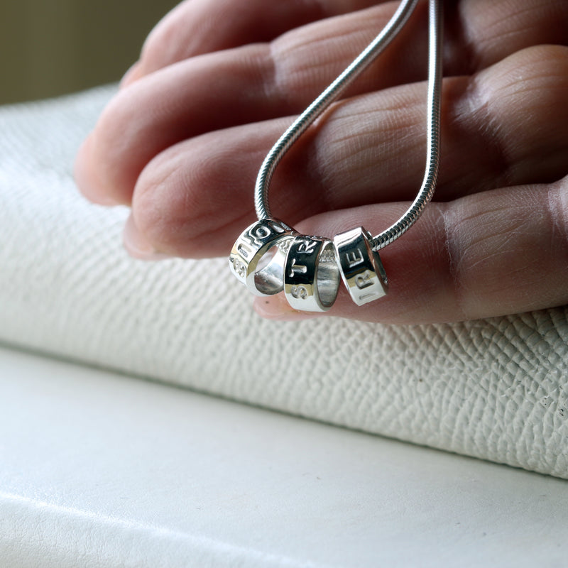 Small hand-stamped silver Memo Beads held between fingertips