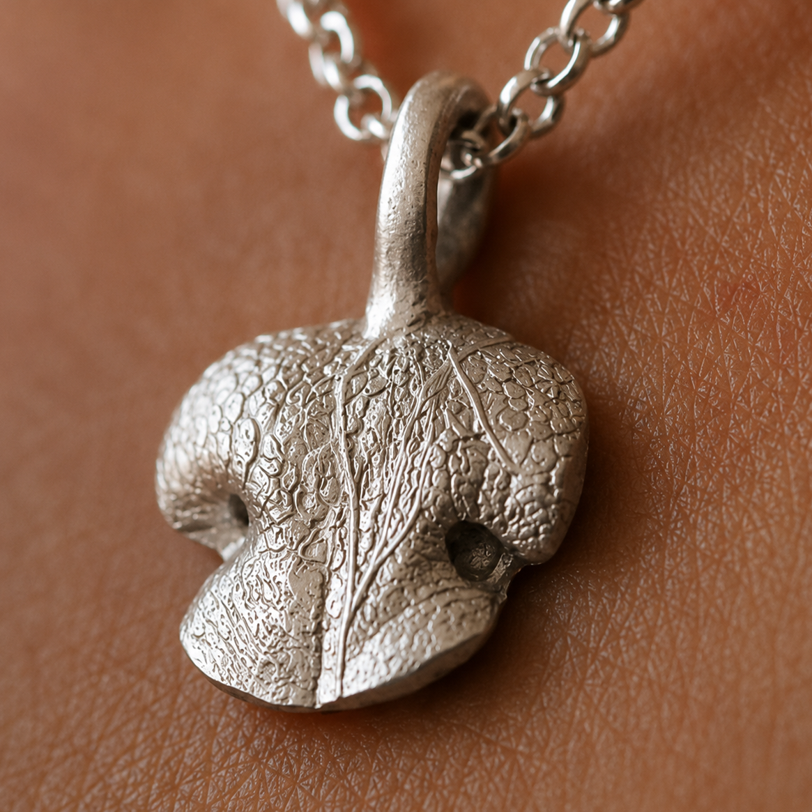 Close-up of a rounded sterling silver Snozza necklace showing the preserved texture of a dog’s nose.