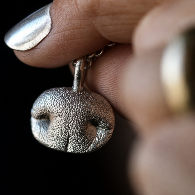 Sterling silver Snozza Oval Dog Nose Impression Necklace held to show the fine texture preserved from a dog nose impression.
