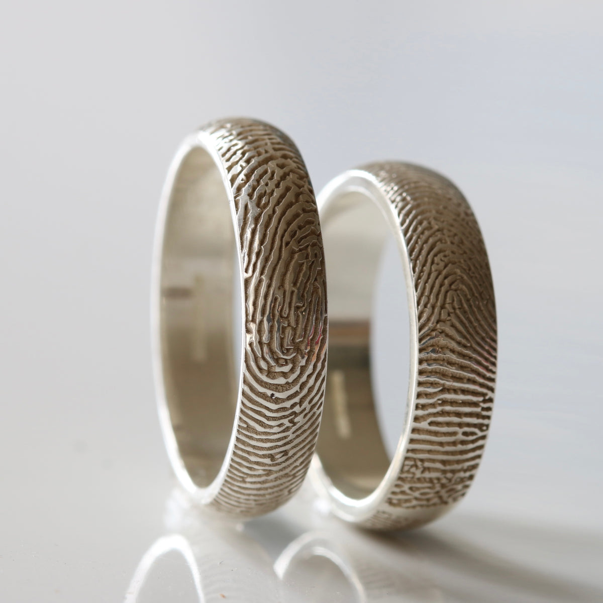 Two silver fingerprint rings standing upright side by side