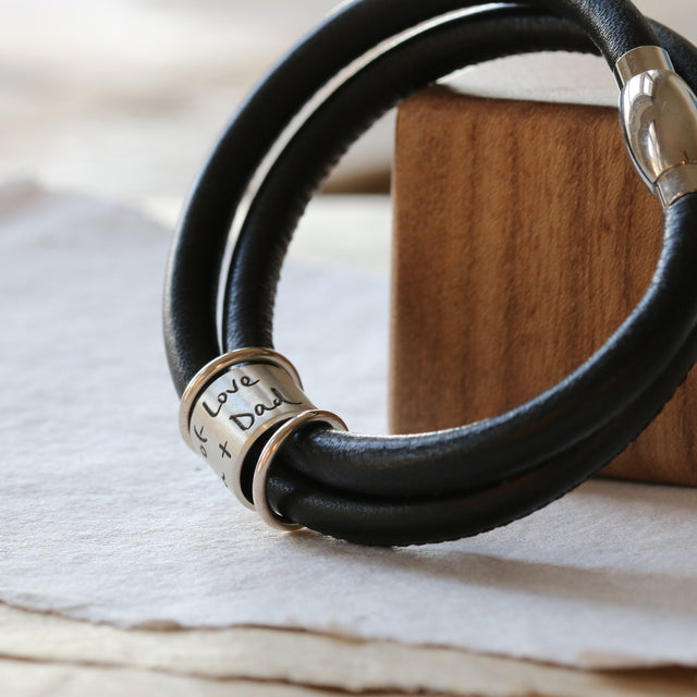 Own Handwriting Story Bead shown on a black leather bracelet.