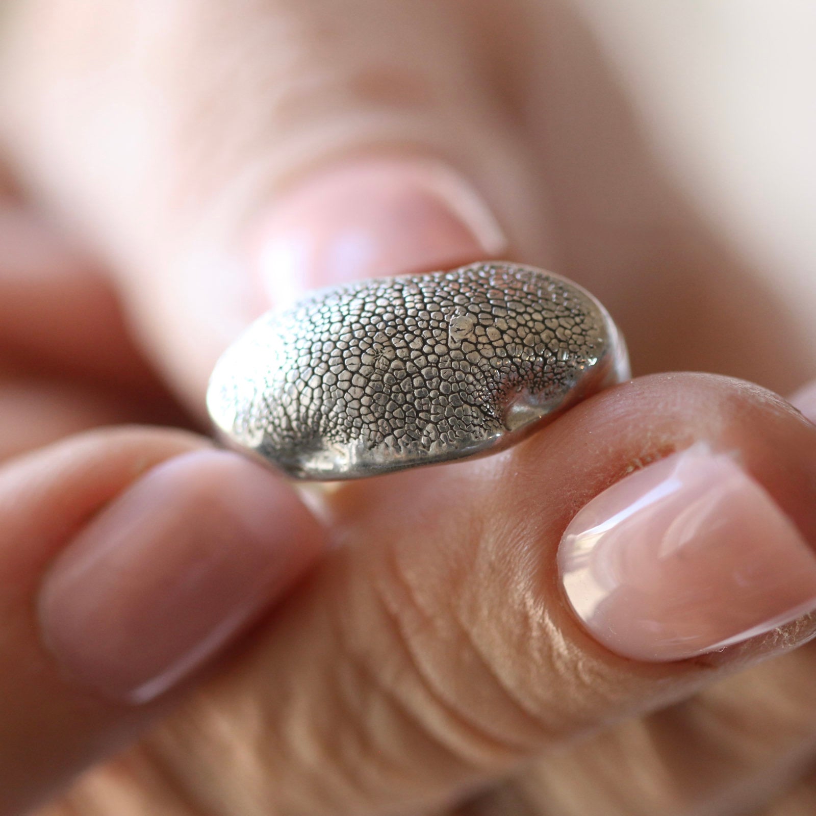 Fuller Silver Snozza dog nose print ring held between fingers, showing its broad textured silver face.