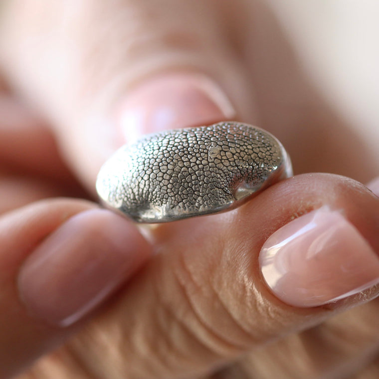 Fuller Silver Snozza dog nose print ring held between fingers, showing its broad textured silver face.