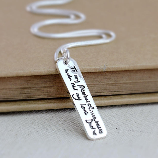 Silver ingot pendant engraved with handwriting, shown on a chain.