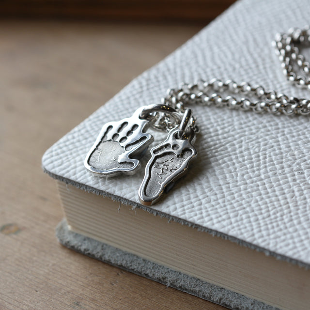 Separate silver hand and footprint charms shown together on a necklace chain.