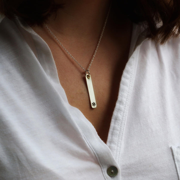 Slim silver medical alert necklace worn with a white blouse