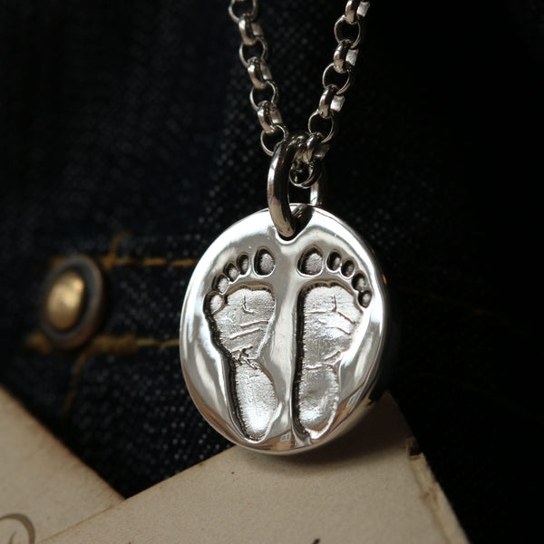 Two footprints reproduced inside a round silver pendant