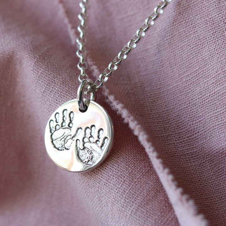 Round silver pendant showing two handprints on fabric