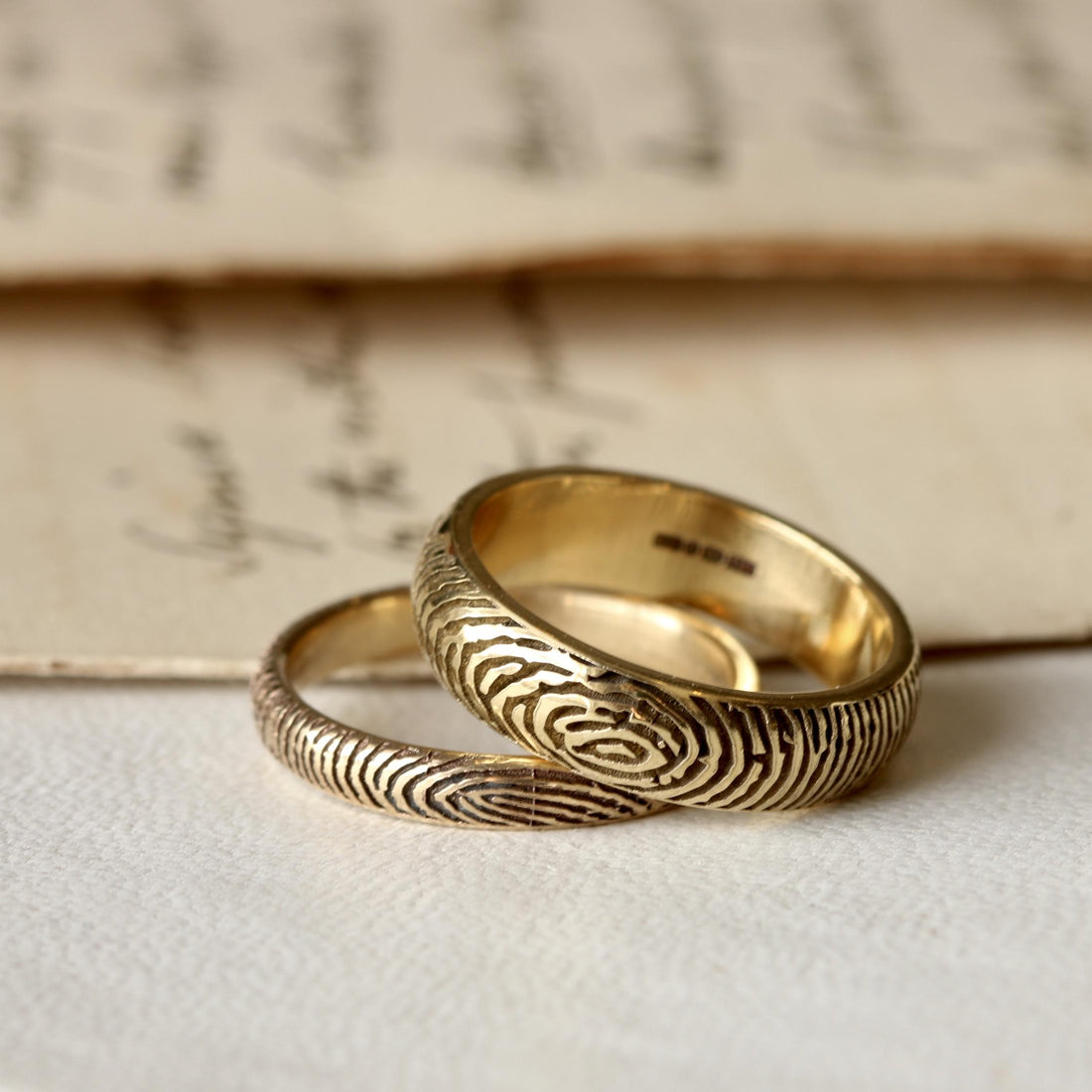 Standard and slender solid gold fingerprint rings beside a handwritten page