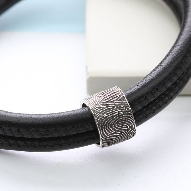 Silver Fingerprint Story Bead shown on a black leather bracelet.