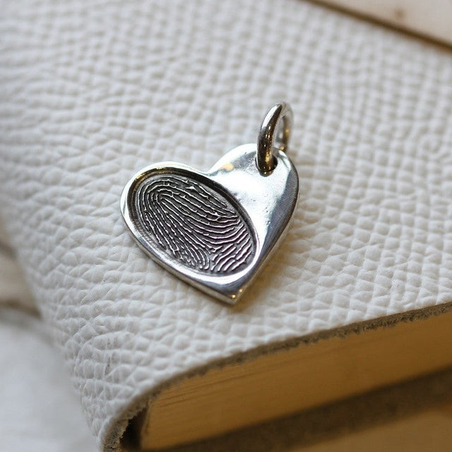 Individual silver heart charm with a fingerprint, photographed on a book.